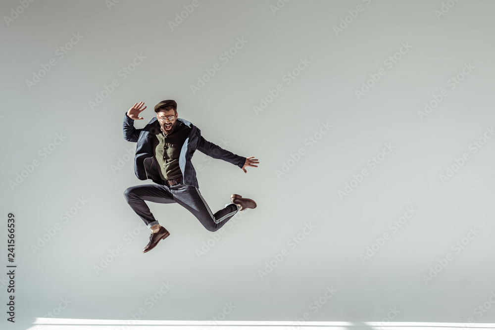 bearded man in cap and glasses jumping high on grey background