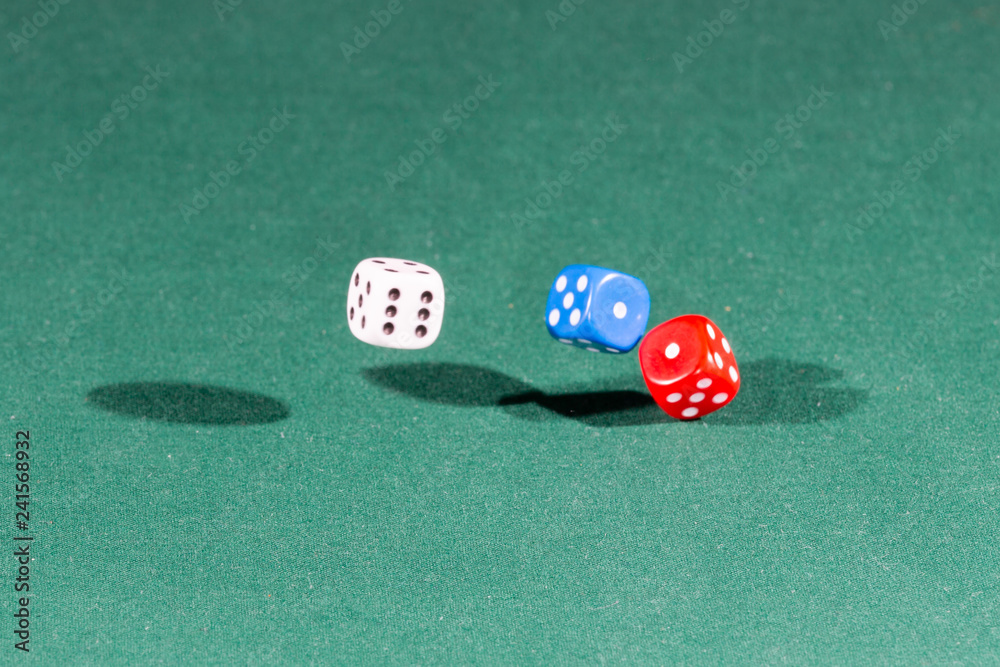 White, red and blue dices falling on a green table White, red and blue dices falling on a green table