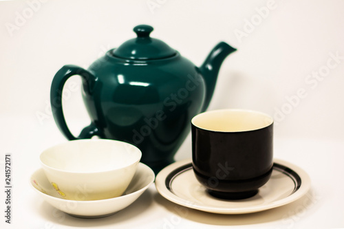 Tea kettle ceramic dark green and two tea cups with saucers on a white background