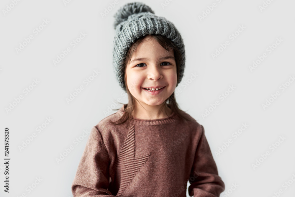 Cute happy little girl in the winter warm gray hat, wearing sweater posing on a white studio background. Cute happy little girl in the winter warm gray hat, wearing sweater posing on a white studio background.