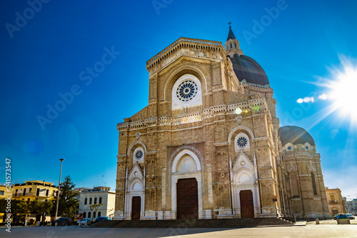 Cathedral of St. Peter the Apostle, also known as Duomo Tonti, by Paolo Tonti. Facade, rose windows, portals, dome and apse. The blinding glare of the sun behind the building. Cerignola, Puglia, Italy