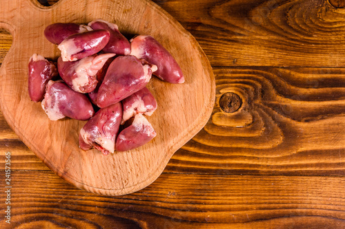 Cutting board with raw chicken hearts on wooden table. Top view