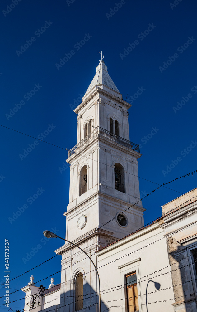Bell tower of the baroque church of the Beata Vergine del Monte Carmelo, Carmine church. White stone, mullioned window, sundial, bell, cross, arch. Cerignola, Puglia, Italy.