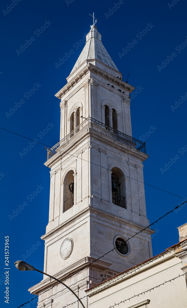 Bell tower of the baroque church of the Beata Vergine del Monte Carmelo, Carmine church. White stone, mullioned window, sundial, bell, cross, arch. Cerignola, Puglia, Italy.