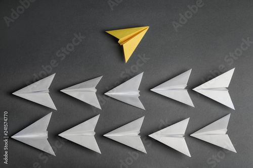 Different color paper plane flying away from others on dark background, top view