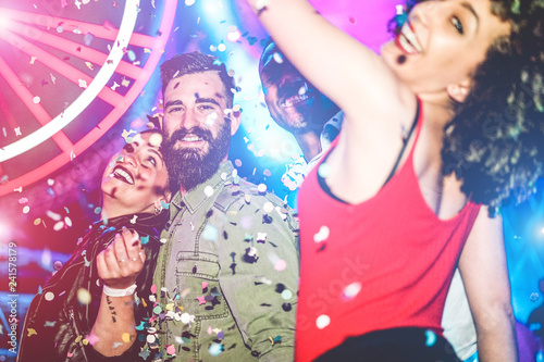 Happy friends dancing at night club festival with laser lights and confetti in background - Focus on left man face
