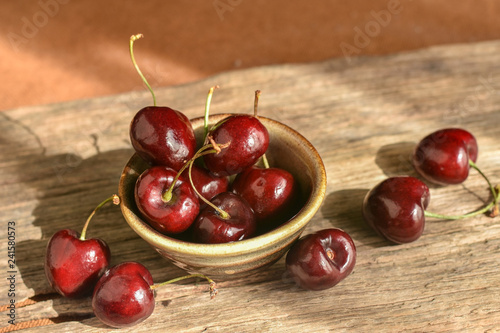 Fresh red ripe cherries in ceramic cup on rustic wood background. Healthy eating and diet organic fruit.