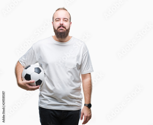 Young caucasian hipster man holding soccer football ball over isolated background with a confident expression on smart face thinking serious