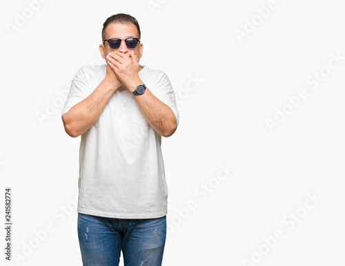 Middle age arab man wearig white t-shirt and sunglasses over isolated background shocked covering mouth with hands for mistake. Secret concept. photo