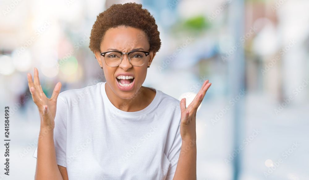 Beautiful young african american woman wearing glasses over isolated background crazy and mad shouting and yelling with aggressive expression and arms raised. Frustration concept. Beautiful young african american woman wearing glasses over isolated background crazy and mad shouting and yelling with aggressive expression and arms raised. Frustration concept.