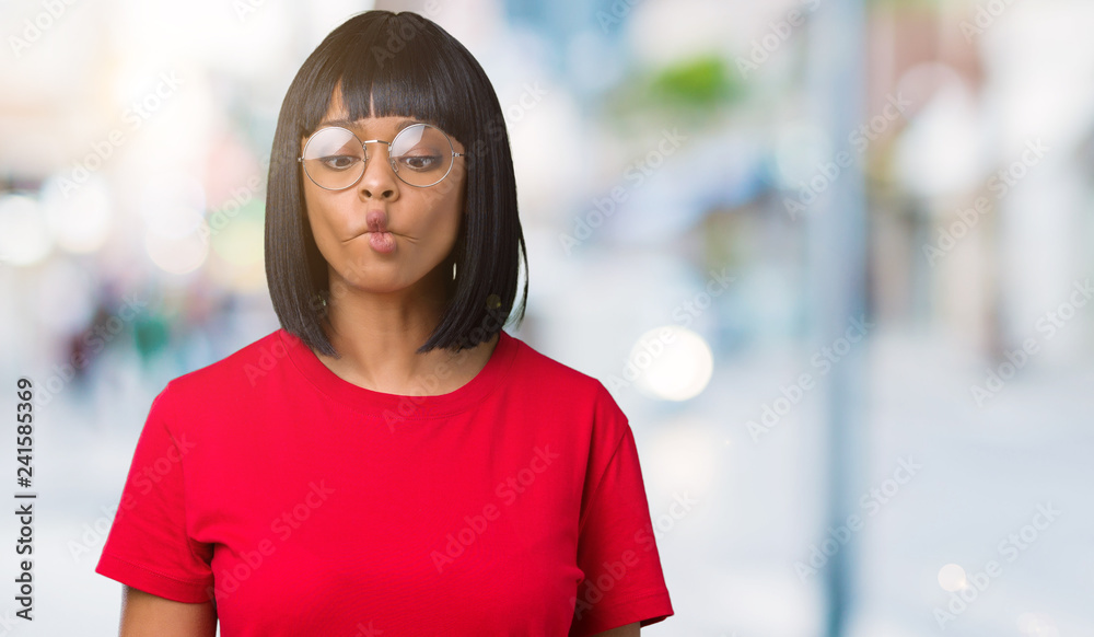 Beautiful young african american woman wearing glasses over isolated background making fish face with lips, crazy and comical gesture. Funny expression.