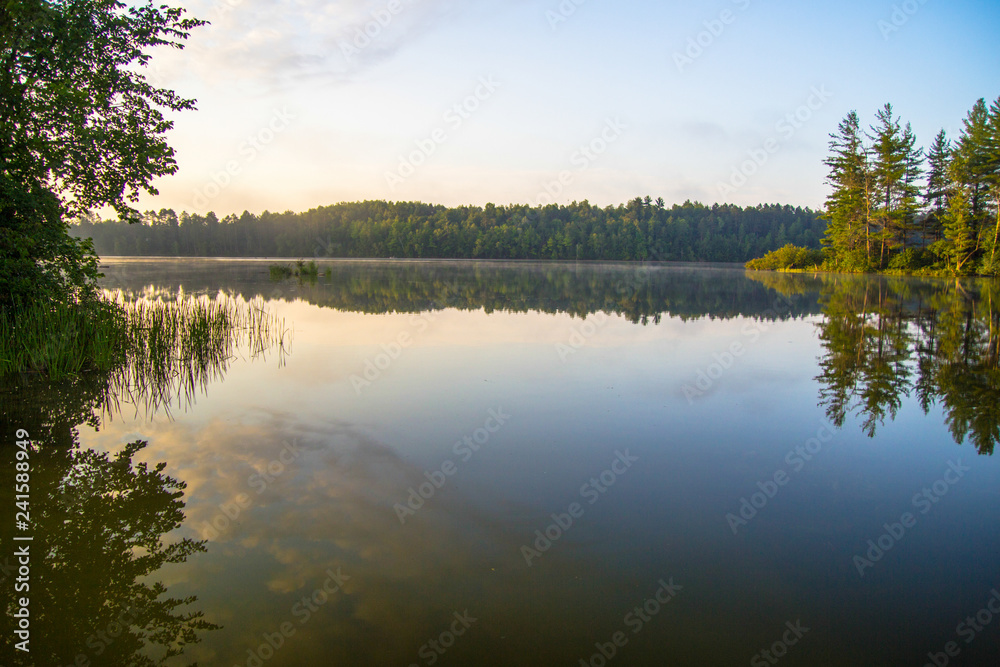 Obraz premium Wilderness Lake Sunrise. Sunlight glows over the horizon of a wilderness lake in northern Michigan. Horizontal orientation with copy space in the foreground.
