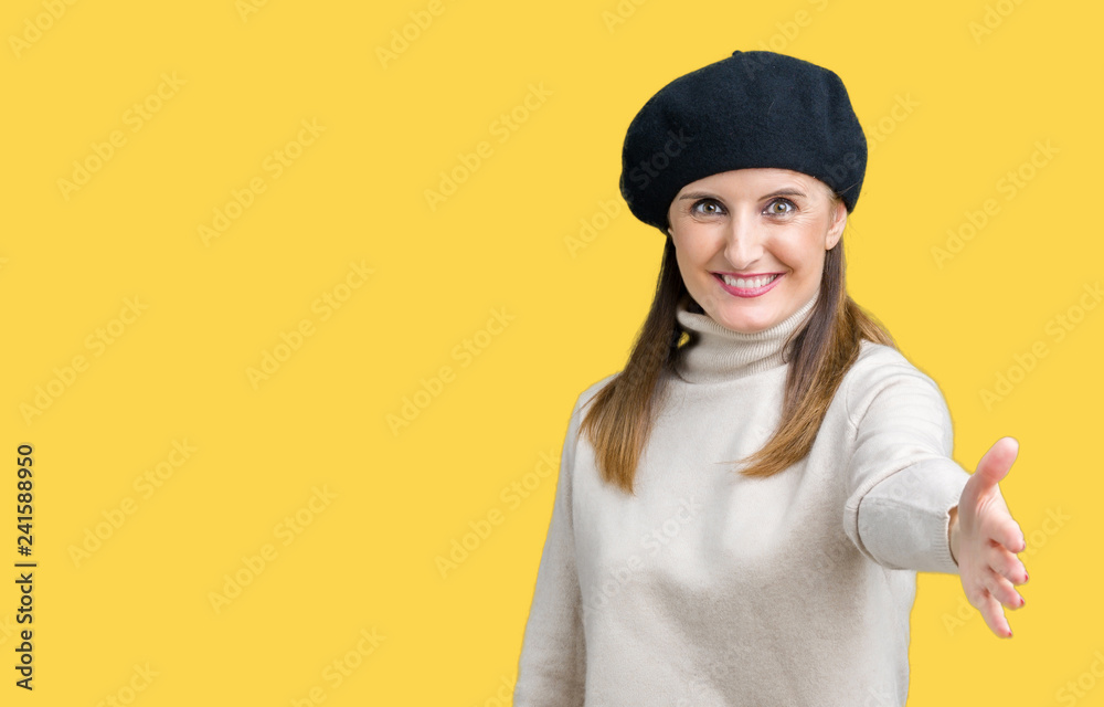 Middle age mature woman wearing winter sweater and beret over isolated background smiling friendly offering handshake as greeting and welcoming. Successful business. Middle age mature woman wearing winter sweater and beret over isolated background smiling friendly offering handshake as greeting and welcoming. Successful business.