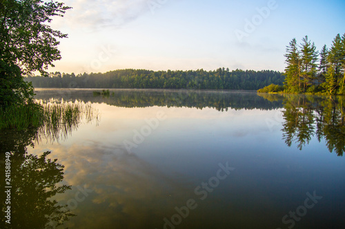 Wilderness Lake Sunrise. Sunlight glows over the horizon of a wilderness lake in northern Michigan. Horizontal orientation with copy space in the foreground.
