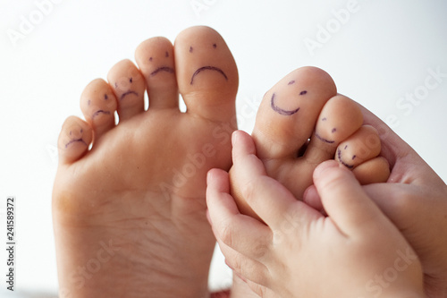 Female toes with painted smileys and children's hands. Foot care concept, pedicure.