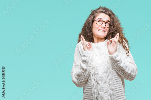 Beautiful brunette curly hair young girl wearing winter sweater over isolated background smiling crossing fingers with hope and eyes closed. Luck and superstitious concept.