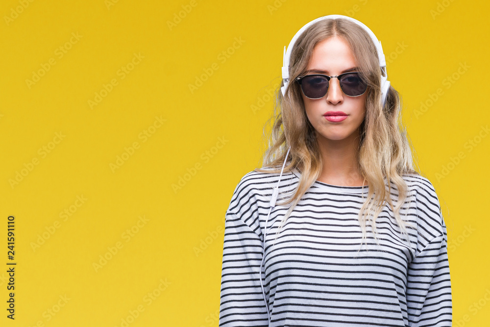 Fototapeta premium Beautiful young blonde woman wearing headphones and sunglasses over isolated background with serious expression on face. Simple and natural looking at the camera.