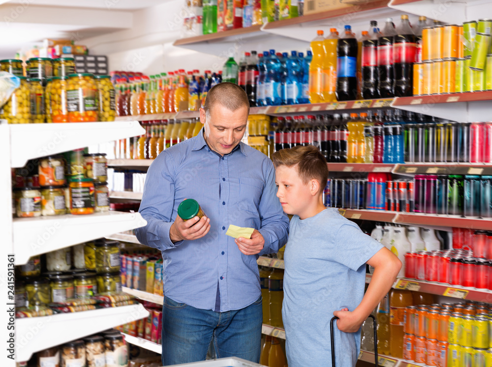 Happy family of father and teen son buying food products on shopping list in supermarket
