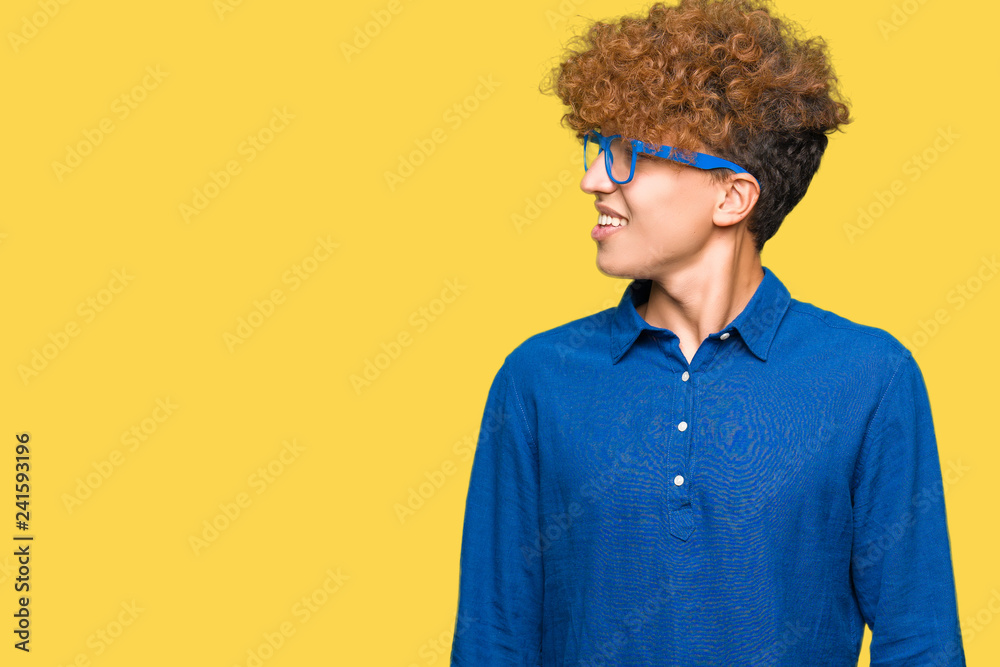 Young handsome man with afro hair wearing blue glasses looking away to side with smile on face, natural expression. Laughing confident. Young handsome man with afro hair wearing blue glasses looking away to side with smile on face, natural expression. Laughing confident.
