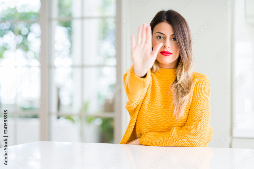 Young beautiful woman wearing winter sweater at home doing stop sing with palm of the hand. Warning expression with negative and serious gesture on the face. Young beautiful woman wearing winter sweater at home doing stop sing with palm of the hand. Warning expression with negative and serious gesture on the face.