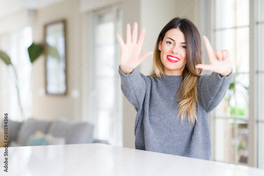 Young beautiful woman wearing winter sweater at home showing and pointing up with fingers number seven while smiling confident and happy.
