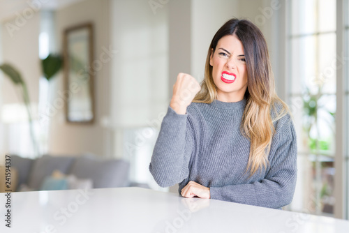 Free Download Young beautiful woman wearing winter sweater at home angry and mad raising fist frustrated and furious while shouting with anger. Rage and aggressive concept. - GFXLoad