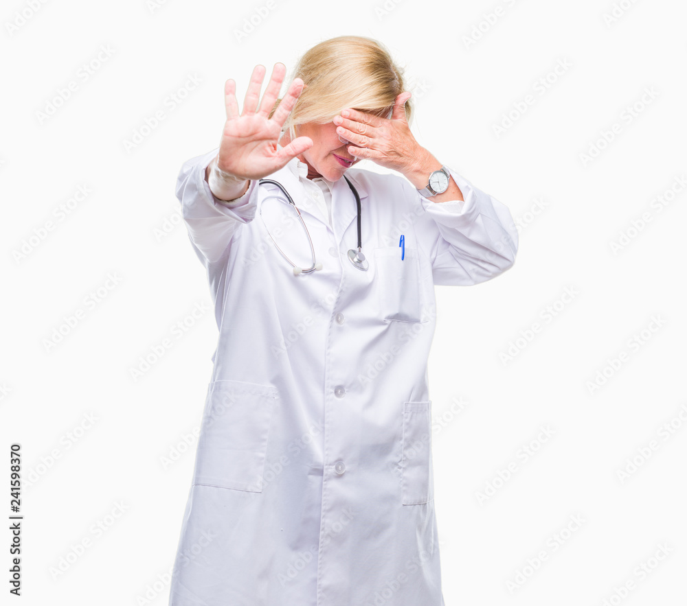 Middle age blonde doctor woman over isolated background covering eyes with hands and doing stop gesture with sad and fear expression. Embarrassed and negative concept. Middle age blonde doctor woman over isolated background covering eyes with hands and doing stop gesture with sad and fear expression. Embarrassed and negative concept.