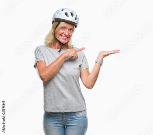 Middle age caucasian cyclist woman wearing safety helmet over isolated background amazed and smiling to the camera while presenting with hand and pointing with finger. © Krakenimages.com