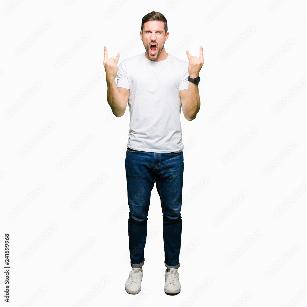 Handsome man wearing casual white t-shirt shouting with crazy expression doing rock symbol with hands up. Music star. Heavy concept. Handsome man wearing casual white t-shirt shouting with crazy expression doing rock symbol with hands up. Music star. Heavy concept.