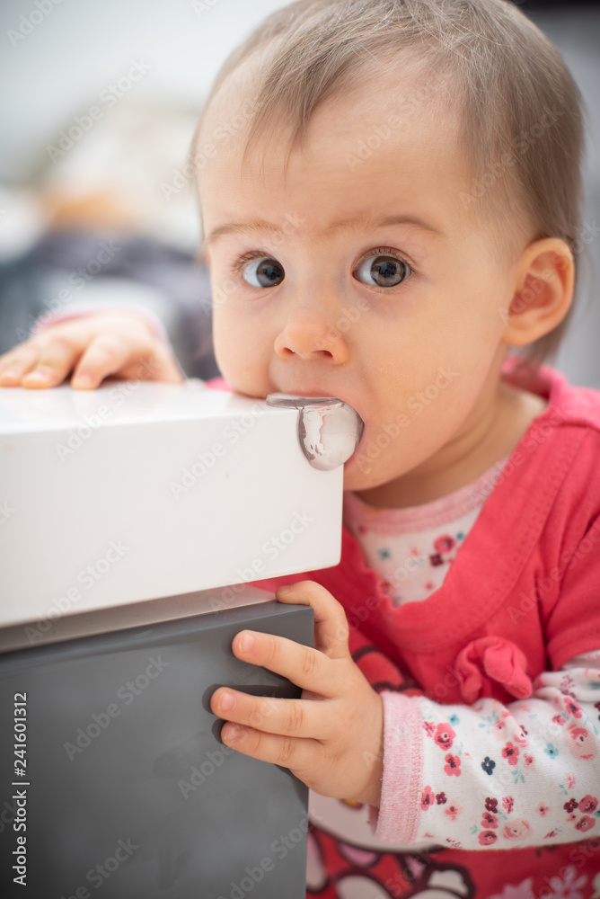 Cute caucasian 1 year old baby girl bites silicon corner protector, concept of teething, Child bites furniture Cute caucasian 1 year old baby girl bites silicon corner protector, concept of teething, Child bites furniture