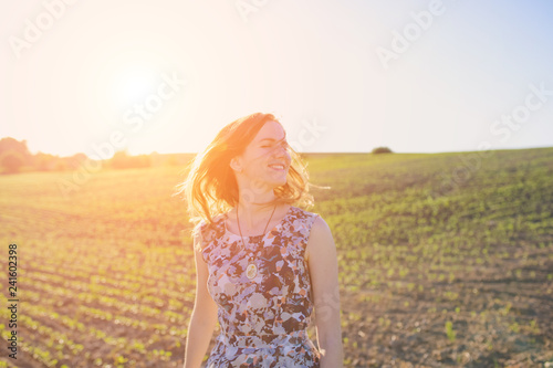 Girl in rustic dress is standing in the field with seed beds. Beautiful woman is turning her head in the sunset lights. Wind in her hair. Eco friendly agriculture modern ideas.
