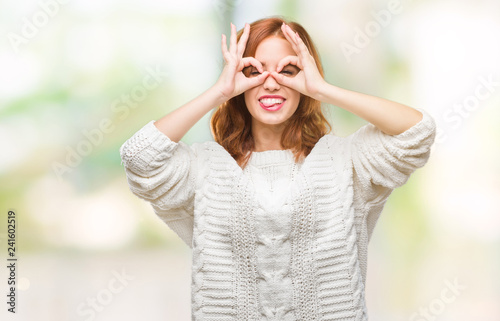 Young beautiful woman over isolated background wearing winter sweater doing ok gesture like binoculars sticking tongue out, eyes looking through fingers. Crazy expression. © Krakenimages.com