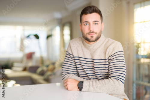 Young handsome man at home with serious expression on face. Simple and natural looking at the camera.