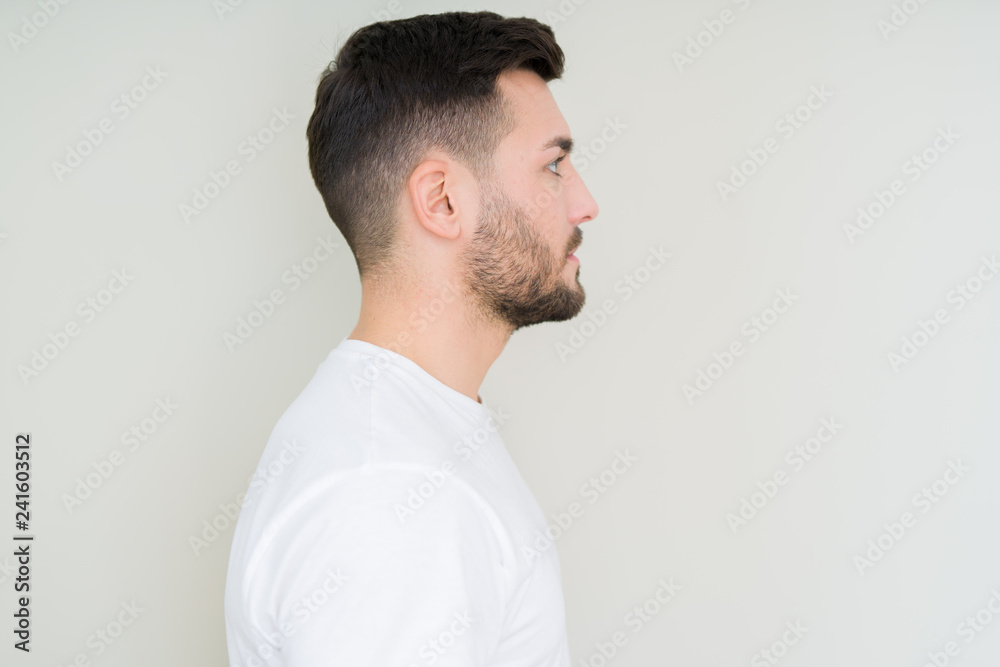 Young handsome man wearing casual white t-shirt over isolated background looking to side, relax profile pose with natural face with confident smile. Young handsome man wearing casual white t-shirt over isolated background looking to side, relax profile pose with natural face with confident smile.