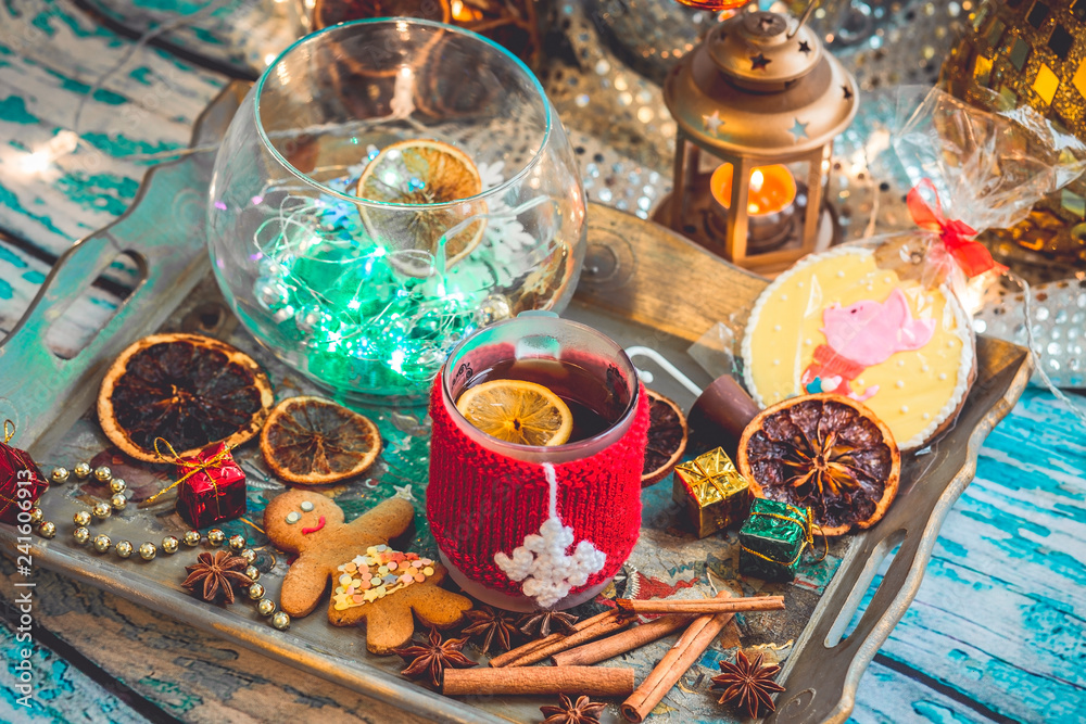 New Year's still life with mug of tea with knitted cup cover, cookies, chocolate, dried fruit and seasonings with lights and bokeh. Photo toned and with vignette