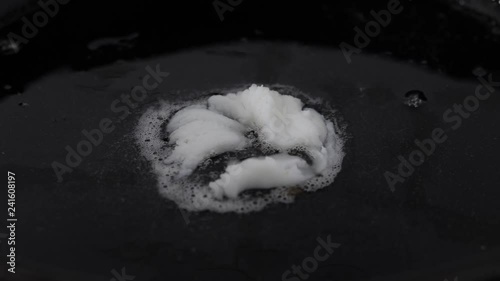 Piece of lard melting on a hot black cast iron pan. Closeup. photo