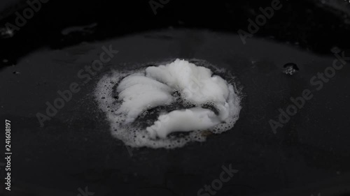 Piece of lard melting on a hot black cast iron pan. Closeup.