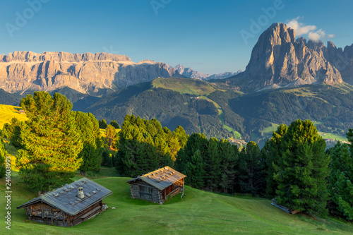 Last rays of sun on traditional huts with view on Sassolungo and Sella Group, Gardena Valley, South Tyrol, Dolomites