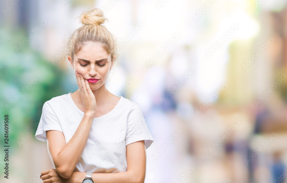 Young beautiful blonde woman wearing white t-shirt over isolated background touching mouth with hand with painful expression because of toothache or dental illness on teeth. Dentist concept.