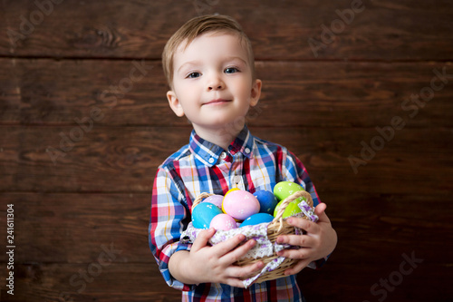 Sticker Happy baby boy with a basket of easter eggs on wooden background