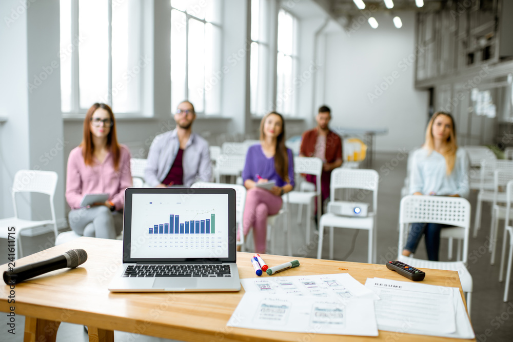 View on the laptop and papers with charts for presentation on the table in the conference room with people sitting on the background