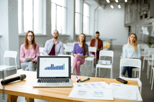 View on the laptop and papers with charts for presentation on the table in the conference room with people sitting on the background