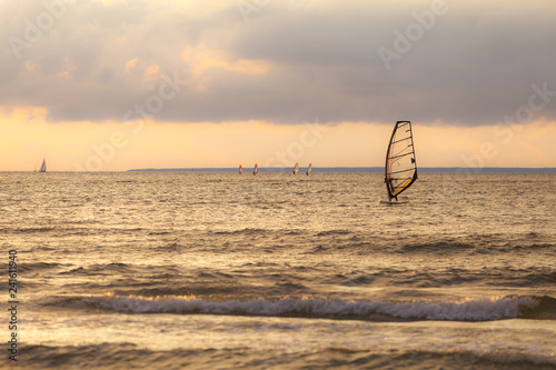 Sportmen windsurfers on the sea surface against sunset orange sky photo