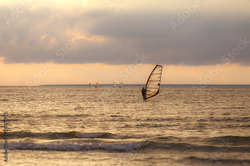 Sportmen windsurfers on the sea surface against sunset orange sky photo