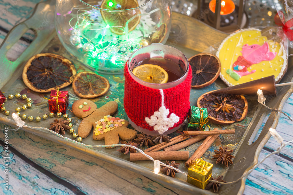 New Year's still life with mug of tea with knitted cup cover, cookies, chocolate, dried fruit and seasonings with lights and bokeh. Photo toned and with vignette