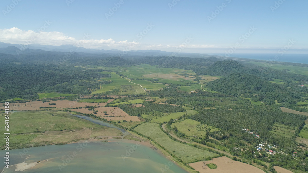 River in mountain valley flowing through farmlands. Aerial view of Mountains with green tropical rainforest, trees, jungle with blue sky. Philippines, Luzon.