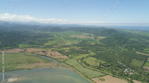 River in mountain valley flowing through farmlands. Aerial view of Mountains with green tropical rainforest, trees, jungle with blue sky. Philippines, Luzon.