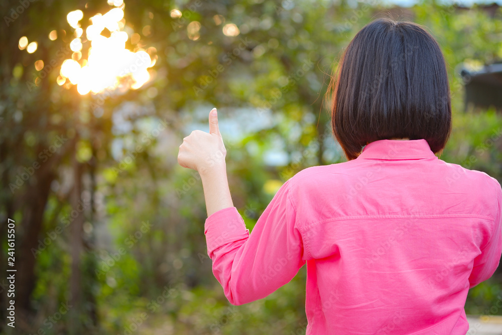 The back of Asian short haired girl holding showing thumbs-up over nature background. Concept Congratulations and encouraging. The back of Asian short haired girl holding showing thumbs-up over nature background. Concept Congratulations and encouraging.