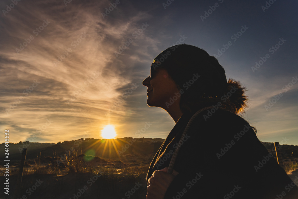 Silhouette face against sunlight of winter wool cap girl with sun in the background of salt glasses. Detail photo of face against light in cold weather