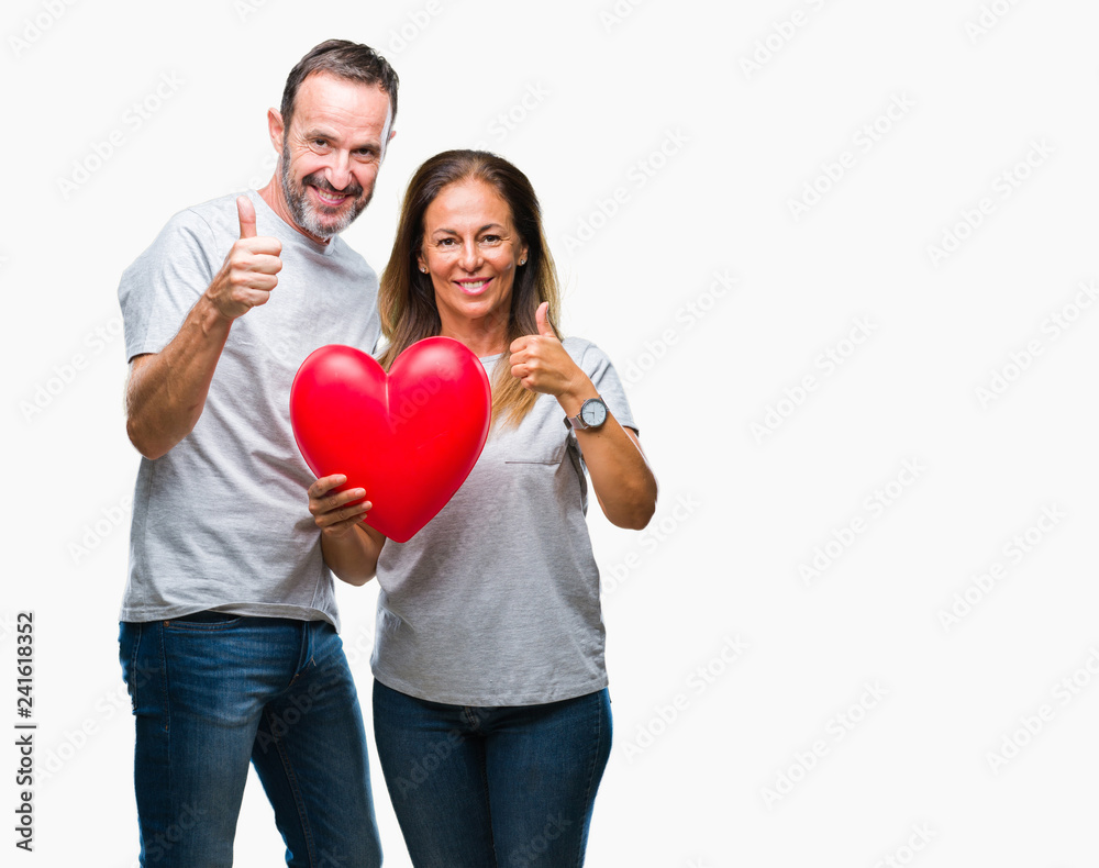 Middle age hispanic casual couple in love holding red heart over isolated background happy with big smile doing ok sign, thumb up with fingers, excellent sign Middle age hispanic casual couple in love holding red heart over isolated background happy with big smile doing ok sign, thumb up with fingers, excellent sign